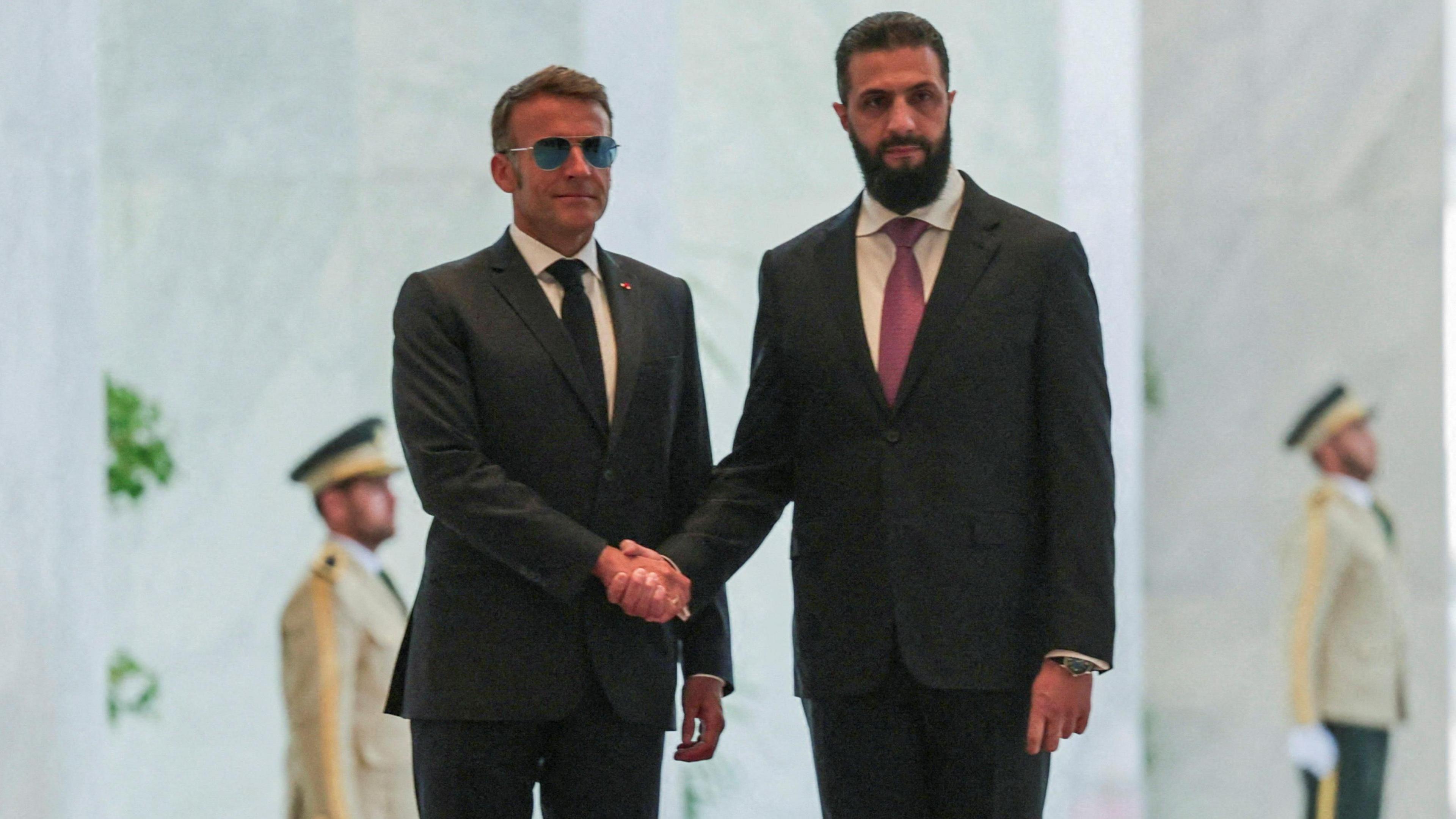 Macron shaking hands with Syrian President Ahmed al-Sharaa