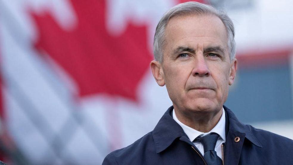 Prime Minister Mark Carney standing next to a Canadian flag